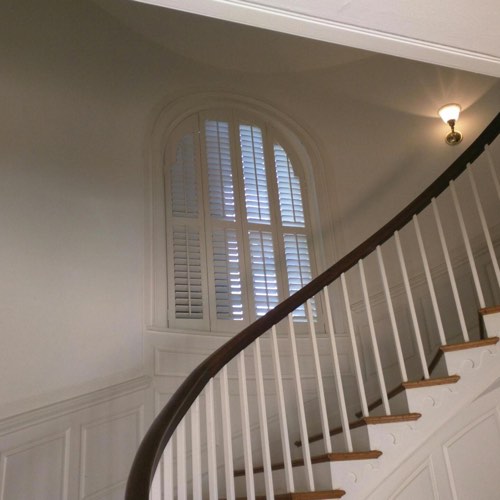 White plantation shutters covering rounded window located in round stairwell.